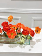 Orange ranunculus poppy daisy fall centerpiece in a clear glass vase