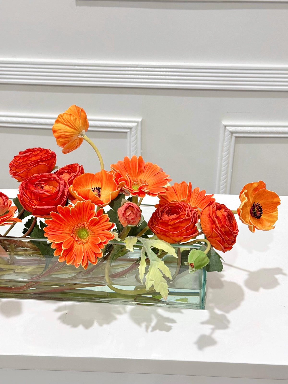 Orange ranunculus poppy daisy fall centerpiece in a clear glass vase