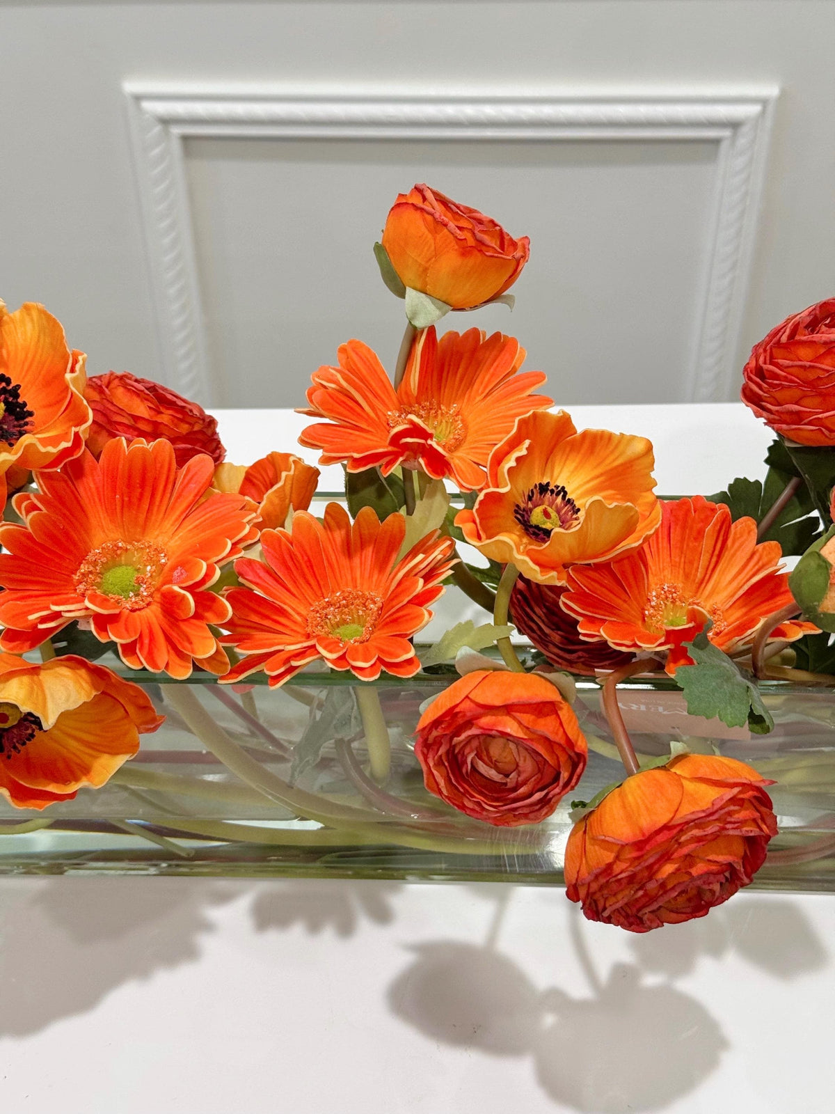 Orange ranunculus poppy daisy fall centerpiece in a clear glass vase
