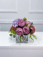 Purple peony rose and hydrangea faux floral centerpiece in a clear glass vase