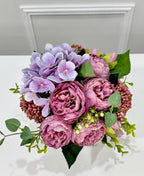 Purple peony rose and hydrangea faux floral centerpiece in a clear glass vase