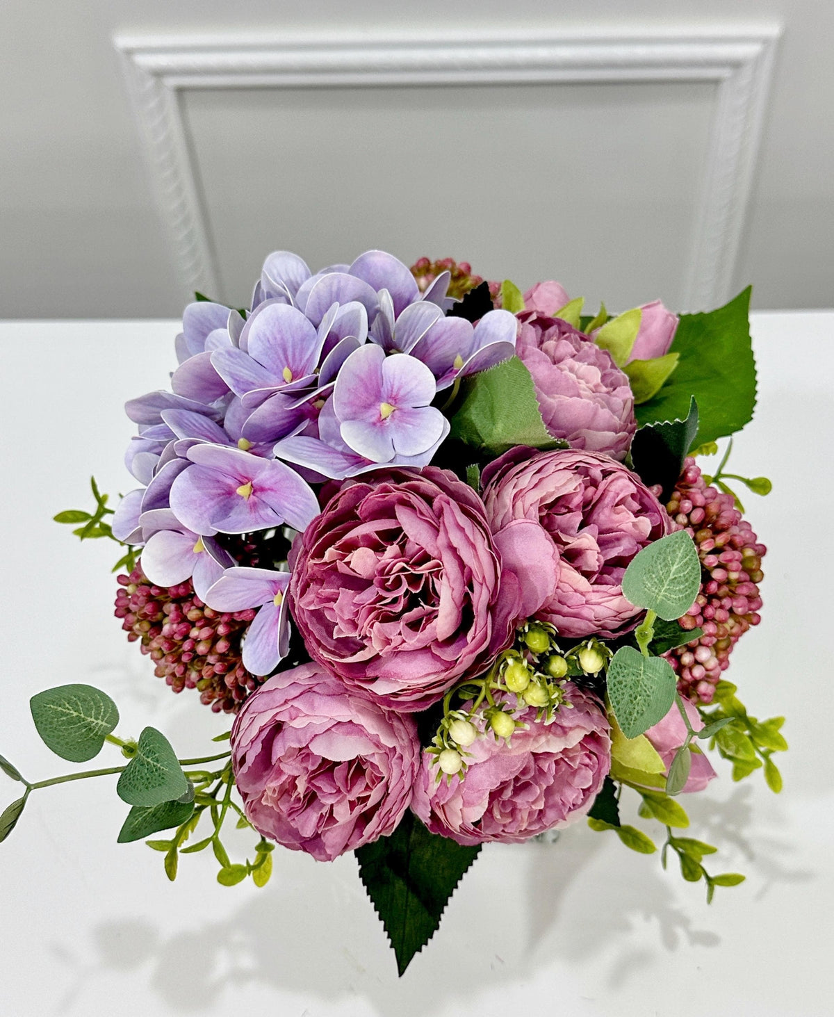 Purple peony rose and hydrangea faux floral centerpiece in a clear glass vase