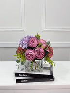 Purple peony rose and hydrangea faux floral centerpiece in a clear glass vase