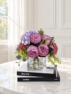 Purple peony rose and hydrangea faux floral centerpiece in a clear glass vase