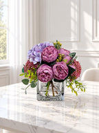 Purple peony rose and hydrangea faux floral centerpiece in a clear glass vase