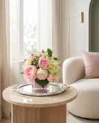 Real touch pink rose and faux hydrangea arrangement in pink cube glass vase on mirrored tray beside boucle sofa