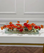 Orange ranunculus poppy daisy fall centerpiece in a clear glass vase
